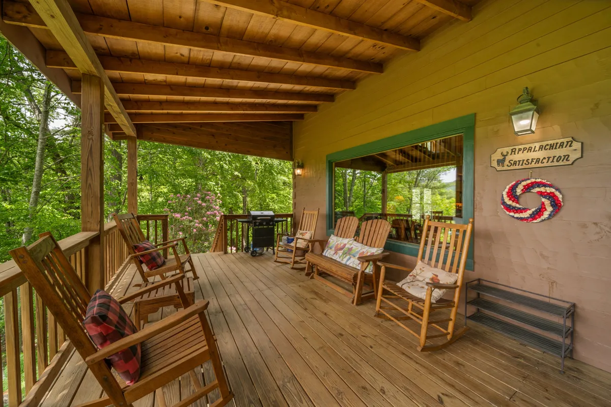 A tranquil deck scene with classic rocking chairs facing greenery, a charming decorative sign, and a wooden deck set amidst the natural landscape. The view accentuates the property's seamless blend of comfort and immersion in the outdoors.