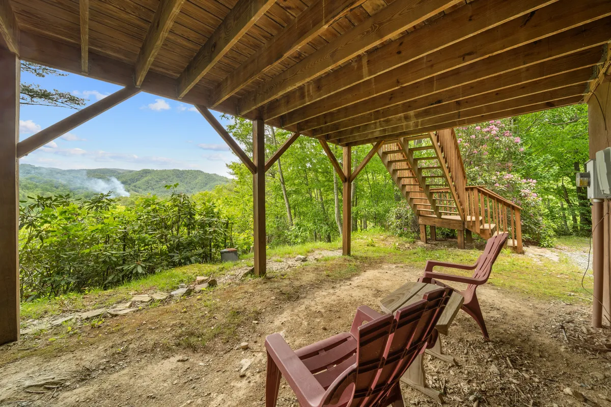 Wooden chairs positioned at the edge of a deck overlook a stunning mountain view, with a staircase leading down to more natural surroundings. The open vantage highlights the property's elevation and direct access to the outdoors.