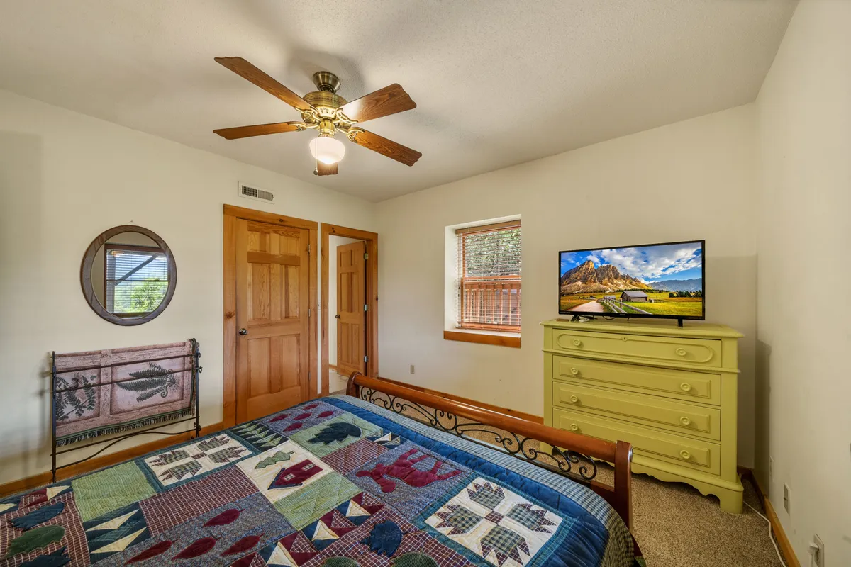 A bright bedroom with a comfortable bed adorned with a quilt, a cheerful yellow dresser, a television, and a large mirror. The space feels cozy and inviting, perfect for a relaxing night's sleep or a lazy morning.
