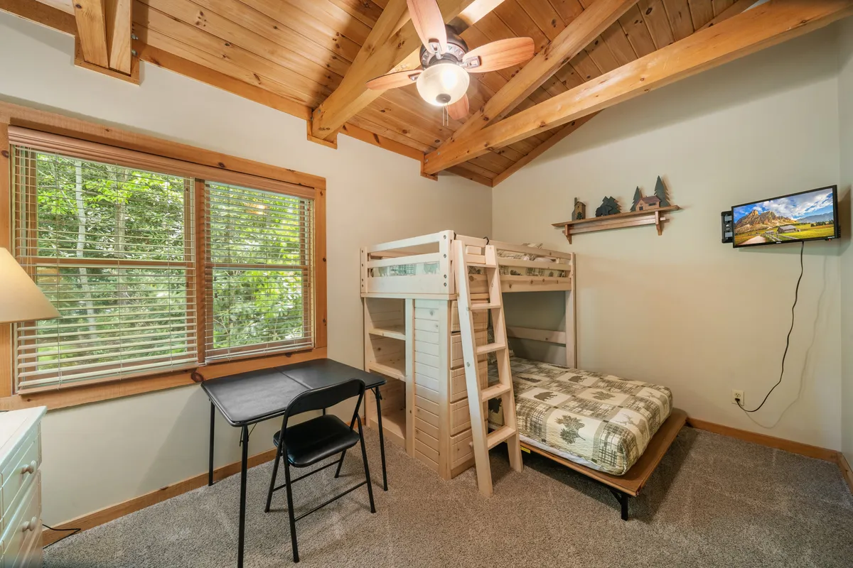 A playful and welcoming kids' bunk room featuring a twin-over-full bunk bed, a desk with a chair for games or study, and a bright window offering greenery views. The space is designed for both fun and relaxation.