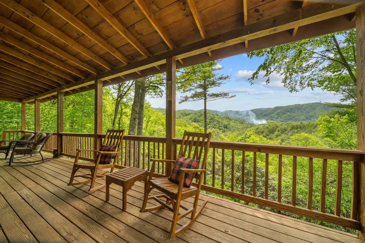 This exterior image features inviting rocking chairs lined up on a wooden deck, overlooking a sweeping mountain view framed by lush green trees. The scene suggests a peaceful spot to take in nature, relax, or socialize outdoors while basking in the surrounding Blue Ridge beauty.