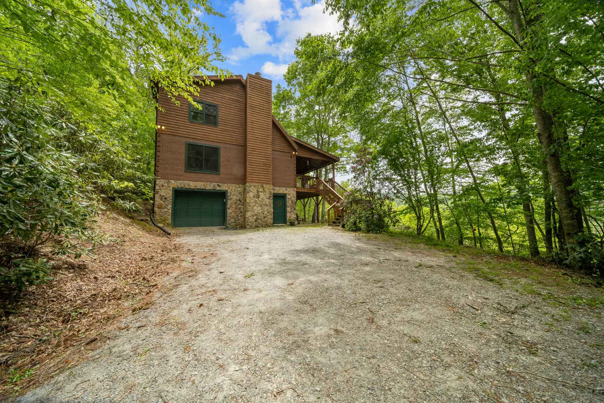 An exterior view of the home, showcasing its unique architectural features, a welcoming front porch, surrounding greenery, and the driveway. The spacious porch is ideal for group gatherings and nature appreciation, setting the stage for memorable arrivals and departures for excursions.