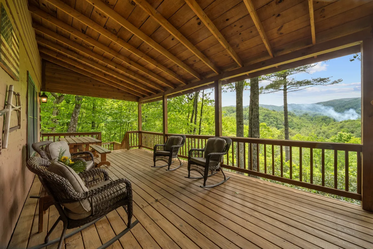 This image features a classic mountain porch with several inviting rocking chairs set on a wooden deck. The porch overlooks lush green surroundings and distant mountain views, offering a peaceful spot for morning coffee or evening relaxation.