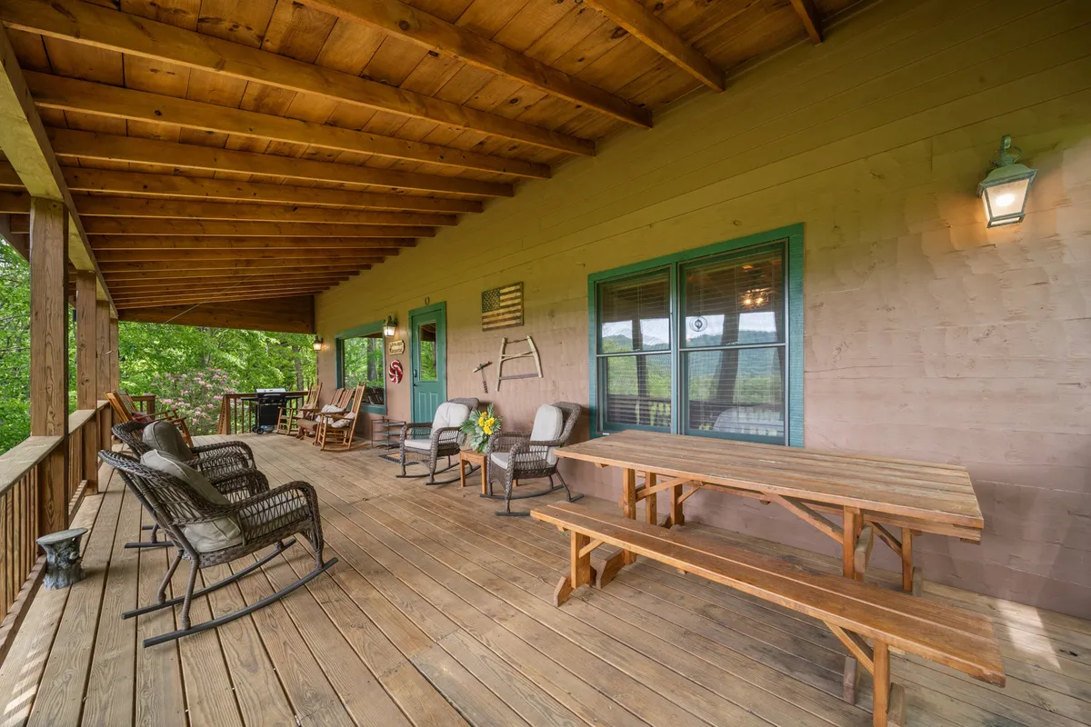 A welcoming porch scene with classic rocking chairs and a wooden table set against rustic green window frames. The porch is decorated with outdoor touches, inviting guests to relax while surrounded by natural beauty and lush greenery.