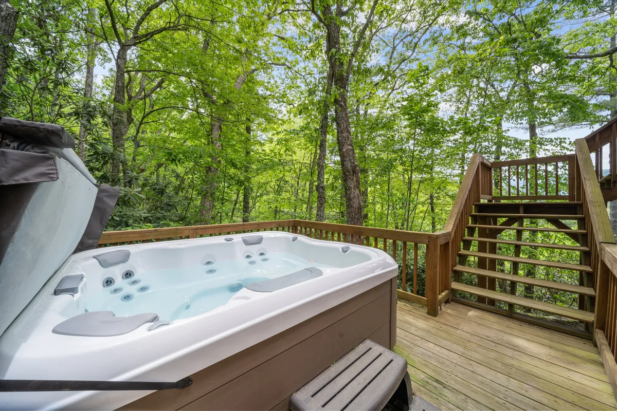 A picturesque view of a bubbling hot tub nestled on a wooden deck, surrounded by leafy trees and natural beauty. The setting is private and tranquil, ideal for relaxation and stargazing after a day of adventure.