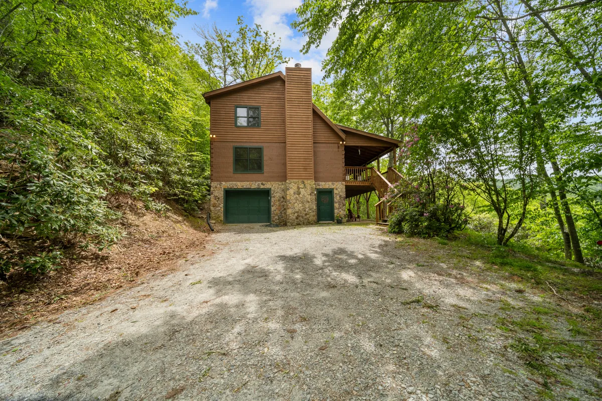 A tranquil exterior view of the cabin featuring its wooden siding, stone foundation, lush surrounding greenery, and a welcoming deck area. The yard invites outdoor activities, nature walks, and group gatherings in a scenic mountain setting.
