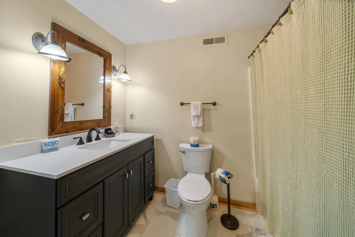 A modern bathroom with dark cabinetry on the vanity, a large framed mirror, and stylish light fixtures. The space feels fresh and functional, ideal for morning routines or evening wind-downs.